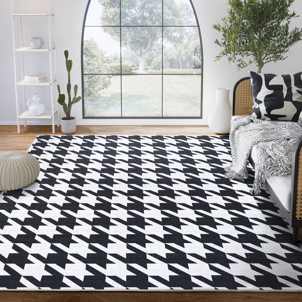 A cream and black geometric houndstooth area rug in a white room with a black couch and a tree.