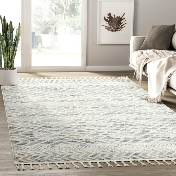 An Abani Cabo Collection beige and gray area rug with a geometric diamond pattern and fringes on the floor.