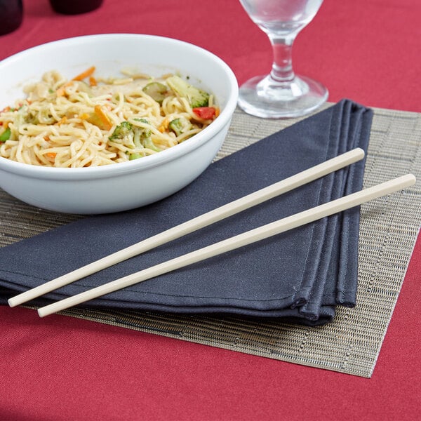 A bowl of noodles with Town ivory plastic chopsticks next to a glass of water.