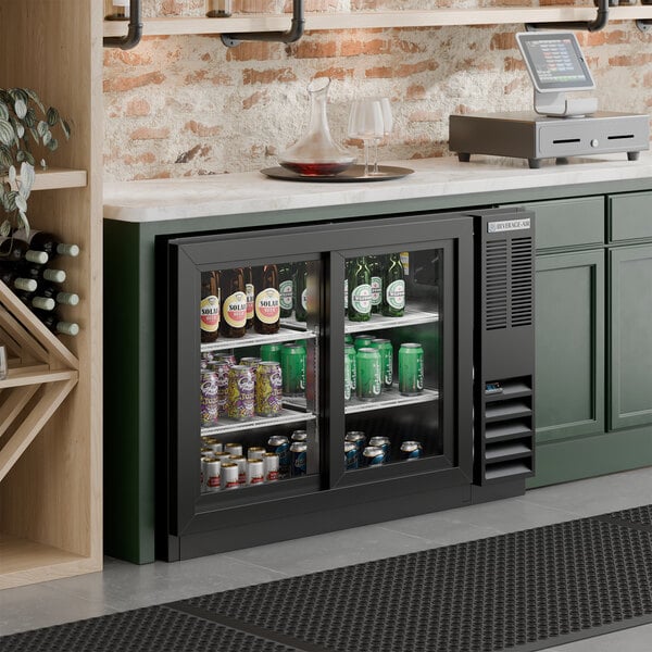 A black underbar height sliding glass door back bar refrigerator filled with assorted beverages.