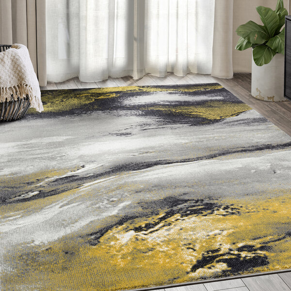 An Abani Arto Collection gold contemporary area rug with a yellow, grey and black abstract design in a room with a white blanket
