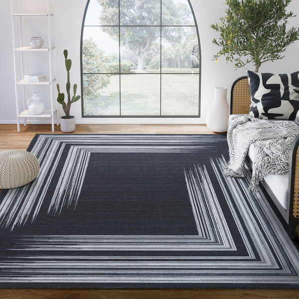 A cream and gray geometric lines area rug in a room with a couch and a plant.