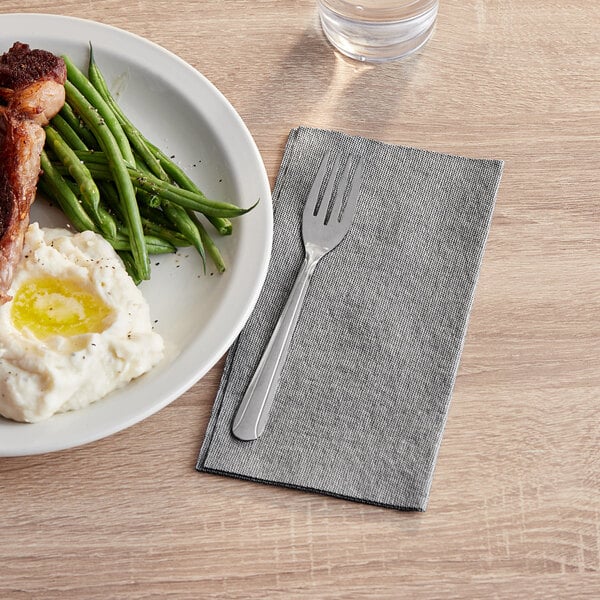 A plate of food with a fork and a black linen-feel dinner napkin on a table.