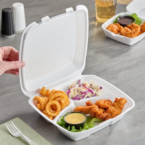 A white foam three-compartment square take out container with a hinged lid, holding fried food, curly fries, coleslaw, and a dipping sauce.