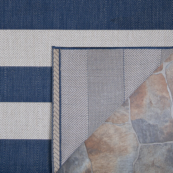 A blue and white striped Couristan Afuera Yacht Club area rug on a stone patio.