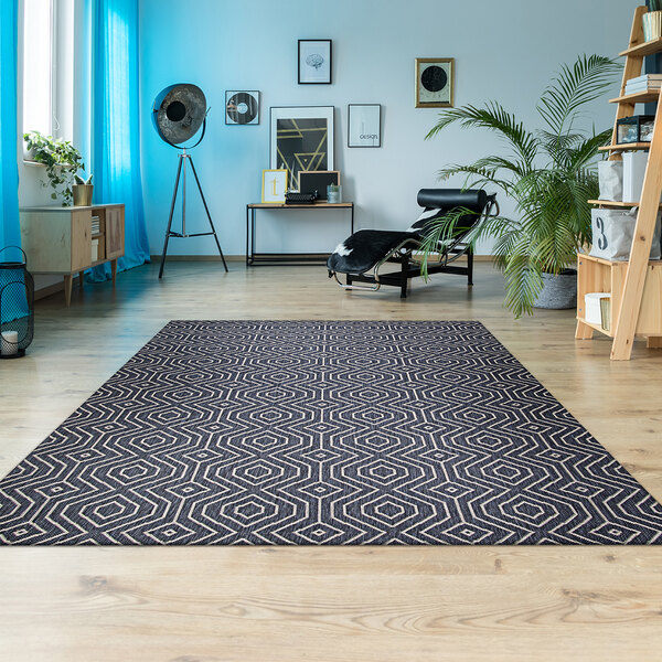 A Couristan Afuera Actinide area rug with a geometric pattern in a room with a chair and a plant on a window sill.