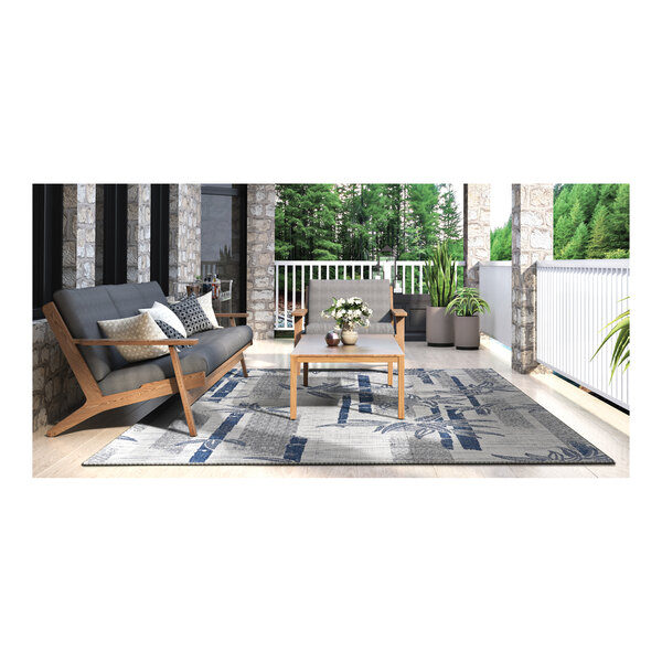 A white and blue Couristan area rug under a table with a vase of white flowers.