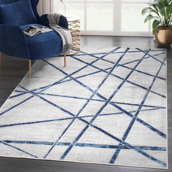 A blue and gray Abani Atlas Collection area rug with criss cross lines in a room with a blue chair.