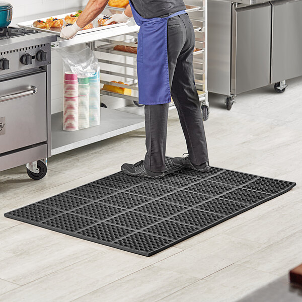 A man standing on a black Lavex anti-fatigue floor mat in a kitchen.