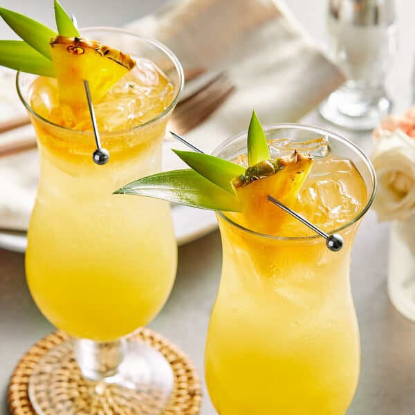 A couple of glasses of drinks with a yellow liquid and pineapple garnish.