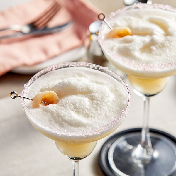 Two martini glasses filled with lychee drinks on a table.