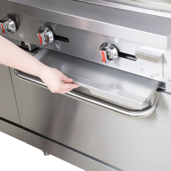 A person holding a silver Main Street Equipment crumb tray over a stove.