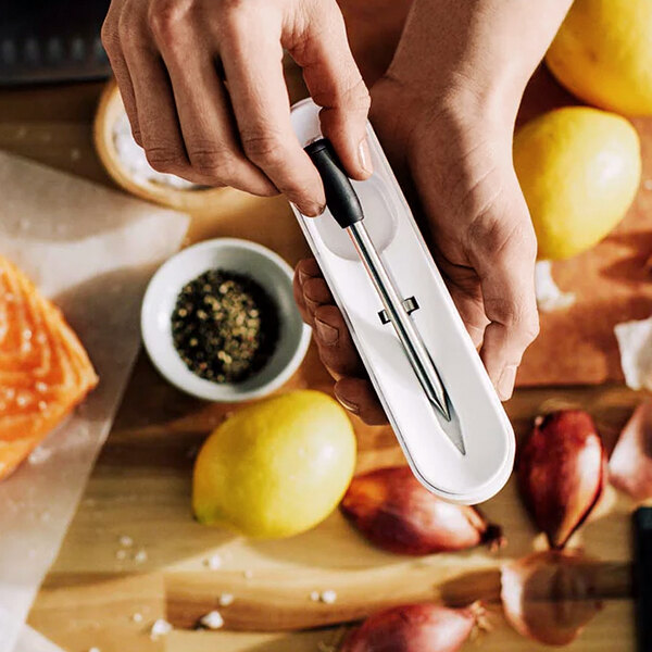 A person's hands using the Yummly Wireless Meat Thermometer to check the temperature of a lemon.
