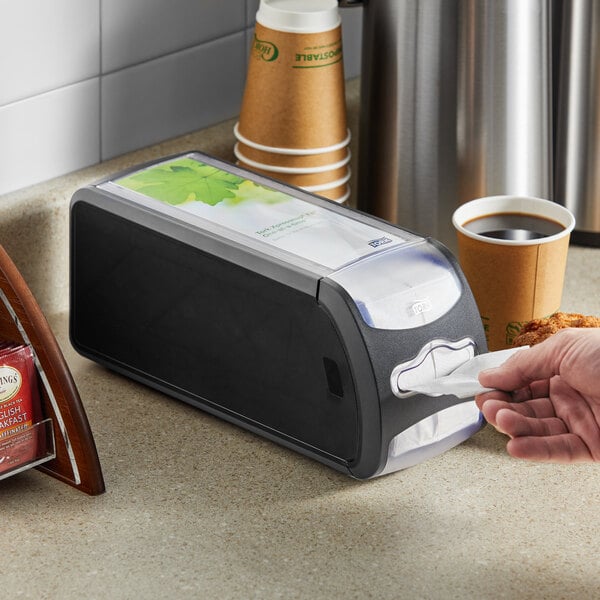 A person using a black Tork countertop napkin dispenser.