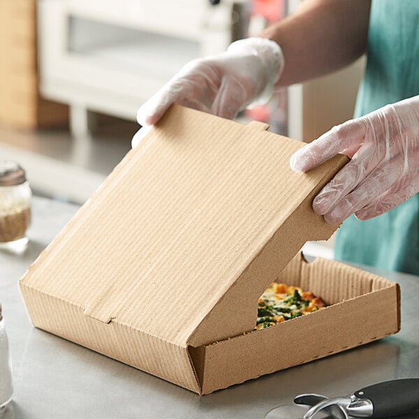 A person in gloves holding a Kraft cardboard pizza box.