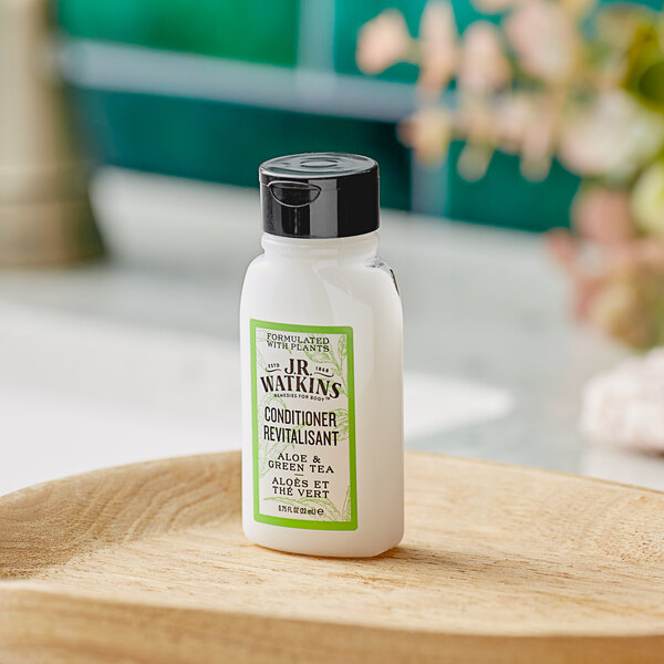 A case of 170 white bottles of JR Watkins Aloe and Green Tea Conditioner with green labels on a wooden surface.