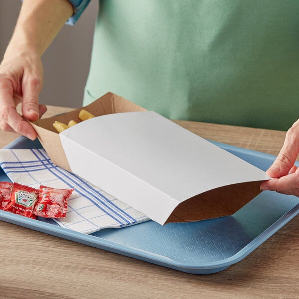 A person holding a white box of french fries on a Carnival King paper food tray.