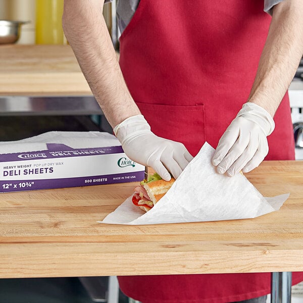 A person in a red apron using Choice Heavy Weight Deli Wrap to wrap a sandwich.