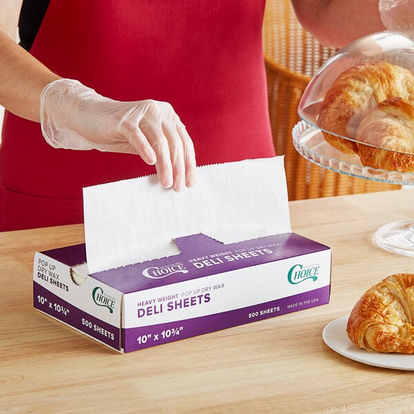 A hand opening a purple and white box of Choice Heavy Weight Interfolded Deli Wrap Wax Paper.