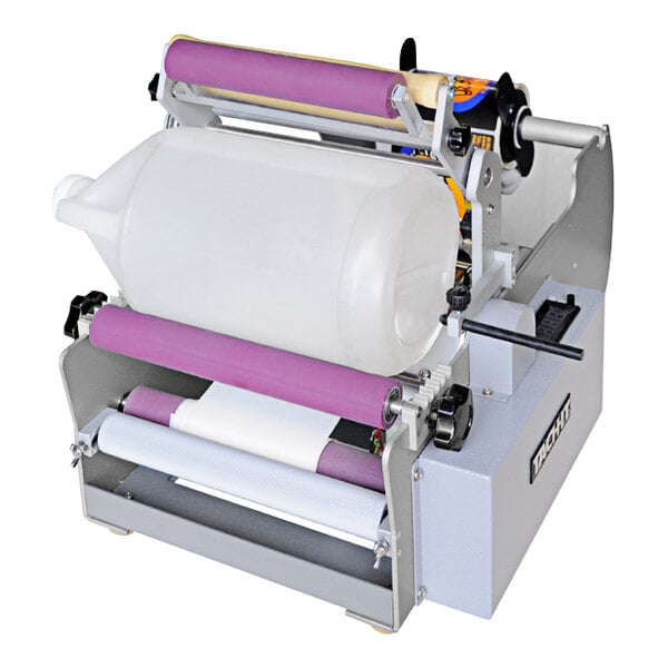 A Tach-It LB7 label applicator applying a label to a white plastic cylinder.