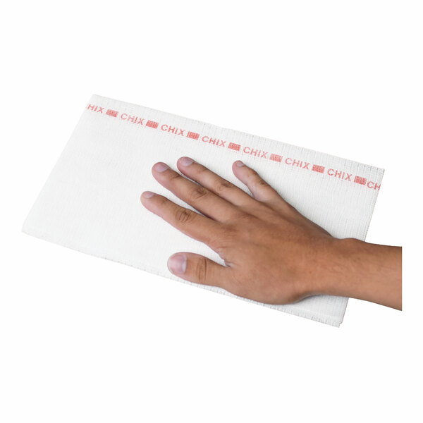 A hand is placed on a rectangular white towel with a red pattern and the word 'CHIX' printed along one edge.