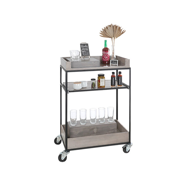 A gray-washed wood Cal-Mil beverage cart with a shelf full of drinks and glasses.
