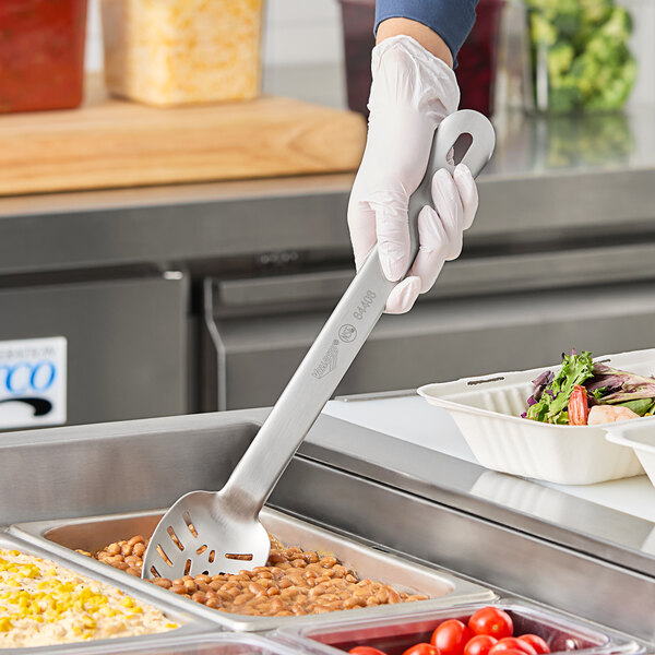 A person in gloves using a Vollrath Jacob's Pride slotted spoon to serve food from a white container.