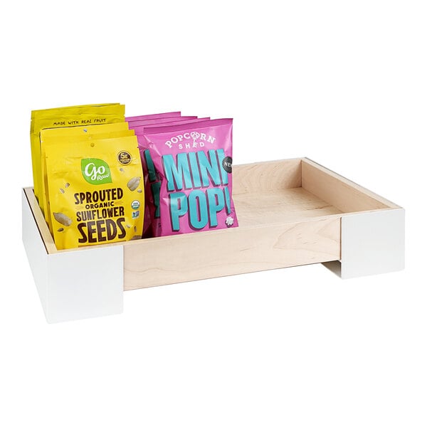 A Cal-Mil maple wood and white metal display merchandiser with bags of sunflower seeds on a wooden tray.