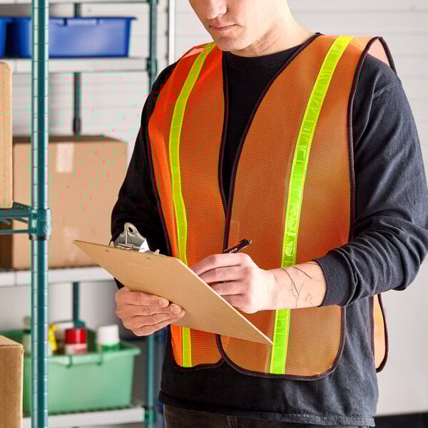 An orange high visibility mesh safety vest with 1-inch reflective tape being worn by a person holding a clipboard.