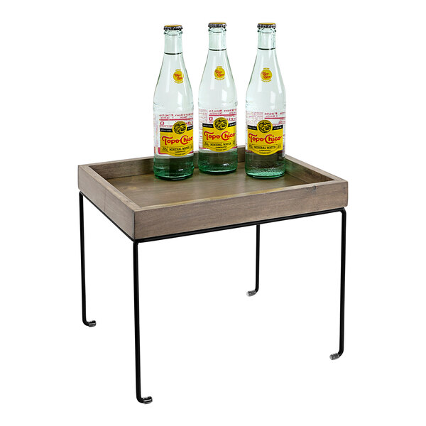 A Cal-Mil gray-washed pine wood display riser with a metal base holding three clear plastic bottles of water on a table.