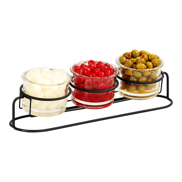 A Cal-Mil black metal condiment display with three glass jars of green olives, red cherries, and white round objects.