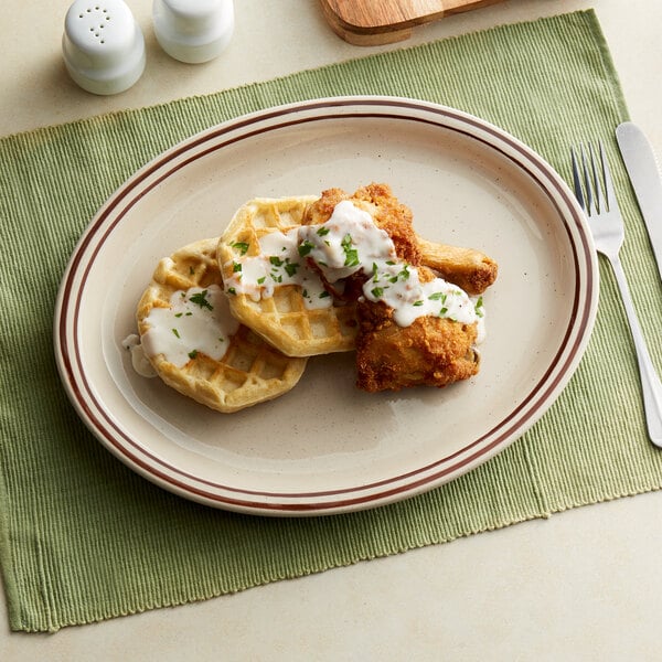 An Acopa brown speckle narrow rim oval stoneware platter with chicken and waffles on it.