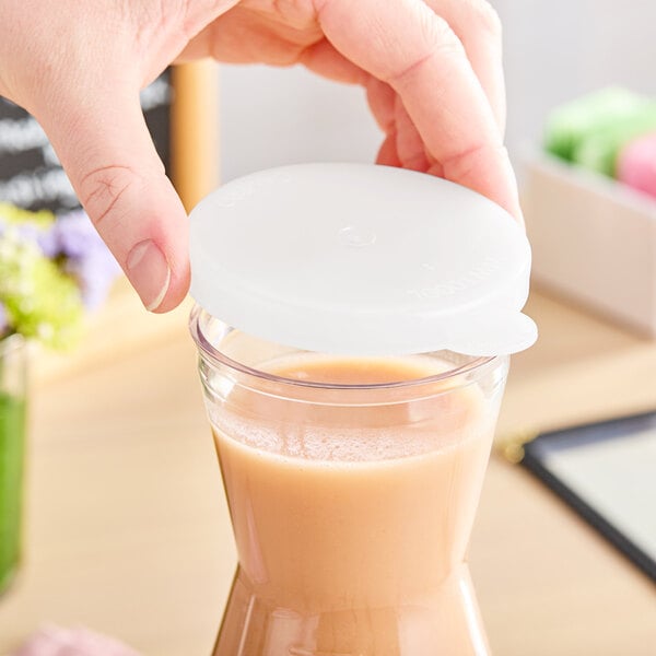 A hand holding a Cambro plastic lid over a glass of liquid.