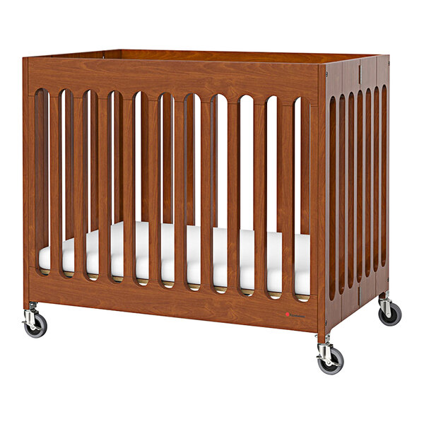 A cherry wood slatted folding crib with wheels.