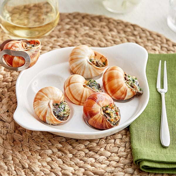 A plate of snails with an Acopa snail fork and a knife on a table.