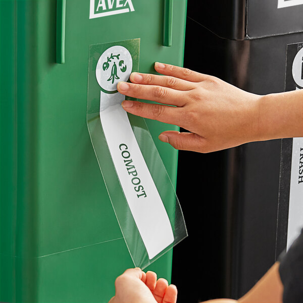 A person's hand using a plastic strip to put a label on a green container.