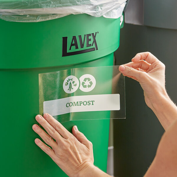 A woman's hand putting a Lavex compost label on a green bin.