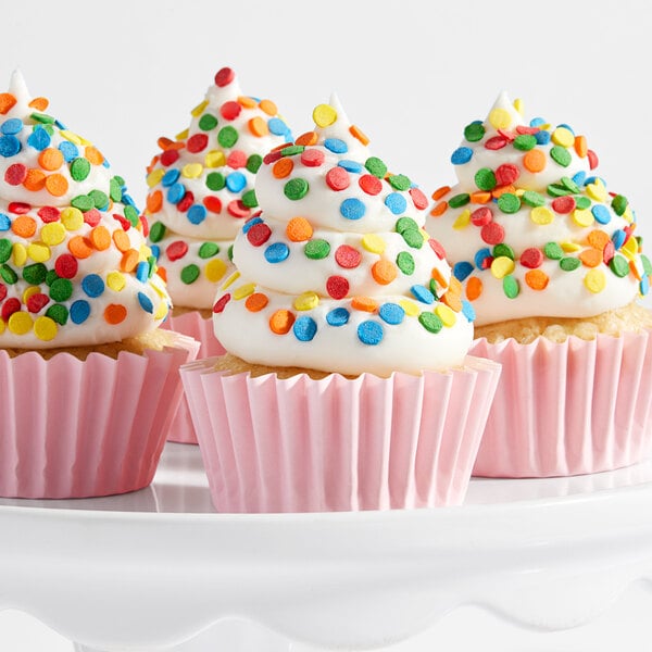 A group of cupcakes with white frosting and colorful confetti sequin sprinkles in pink paper liners.