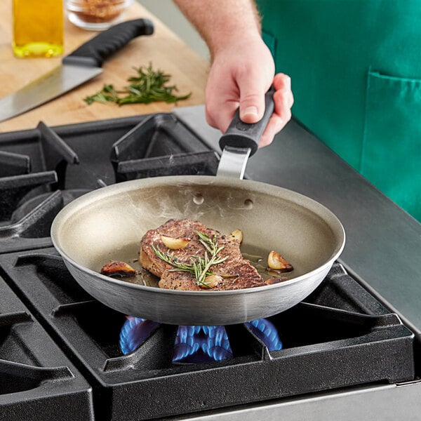A person cooking meat in a Vollrath Wear-Ever non-stick fry pan.