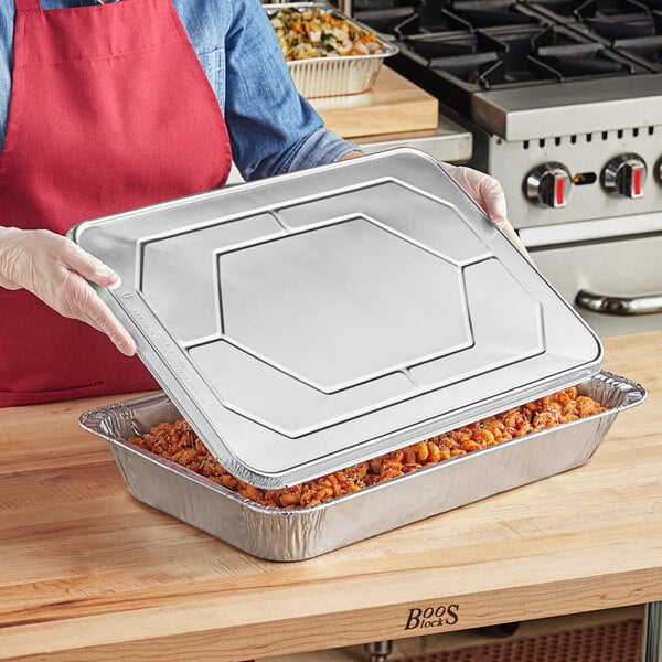 A woman holding a Western Plastics foil steam table pan lid over a tray of food.