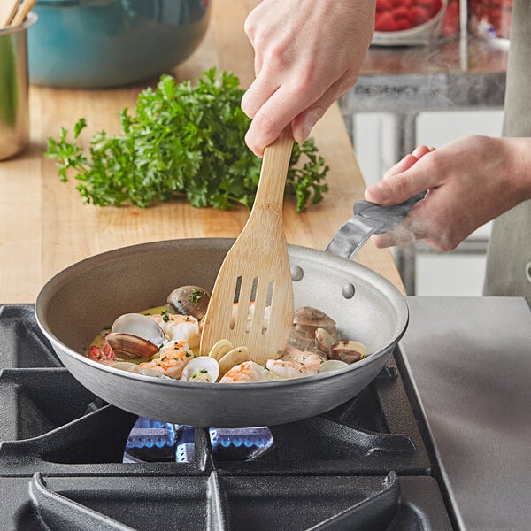 A person cooking seafood in a Vollrath Wear-Ever non-stick fry pan.