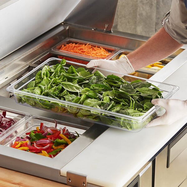 A person in gloves preparing vegetables in a Choice clear polycarbonate food pan on a counter.