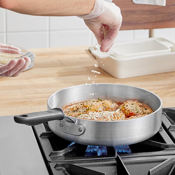 A person pouring rice into a Vollrath Wear-Ever saute pan on a stove.
