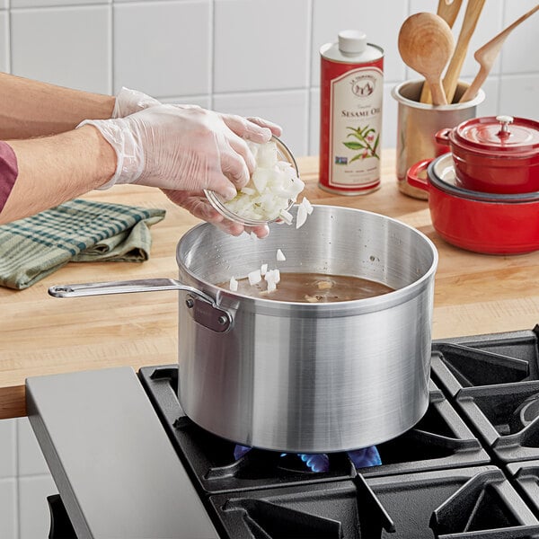 A person pouring chopped onions into a Vollrath aluminum sauce pan.