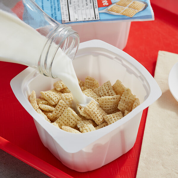 A person pouring milk into a bowl of Rice Chex cereal.