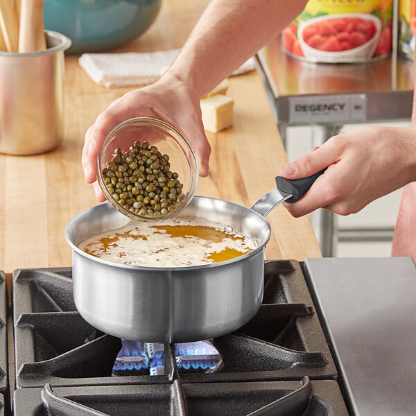 A person pouring food from a Vollrath sauce pan with a black silicone handle.