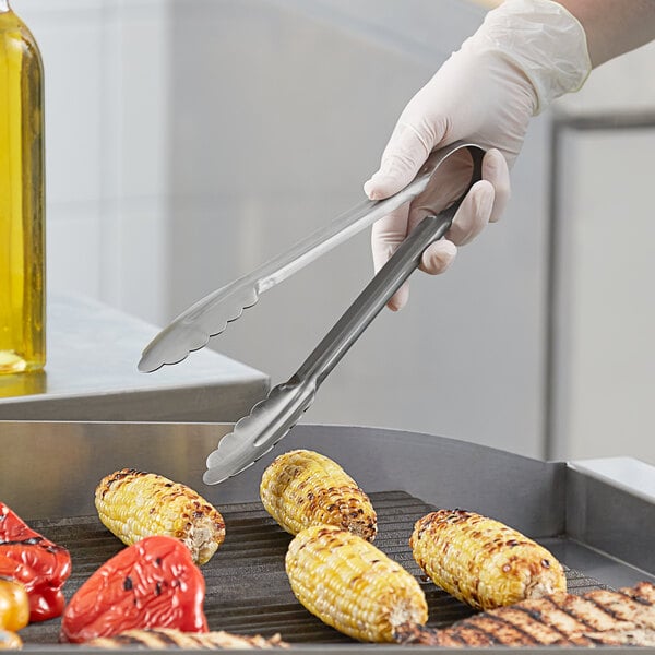 Choice 9 1/2" Heavy-Duty One-Piece Stainless Steel Scalloped Tongs holding a corn on the grill.