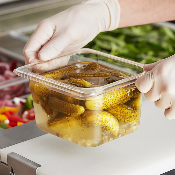A person in gloves holding a Choice clear polycarbonate food pan filled with pickles.