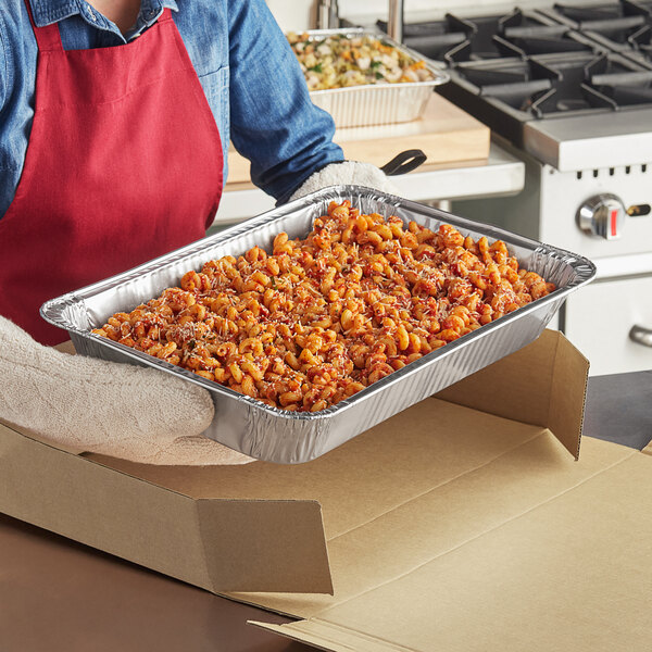 A woman holding a Western Plastics foil steam table pan full of food.