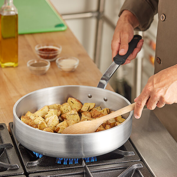 A person cooking food in a Vollrath Wear-Ever saute pan on a stove.